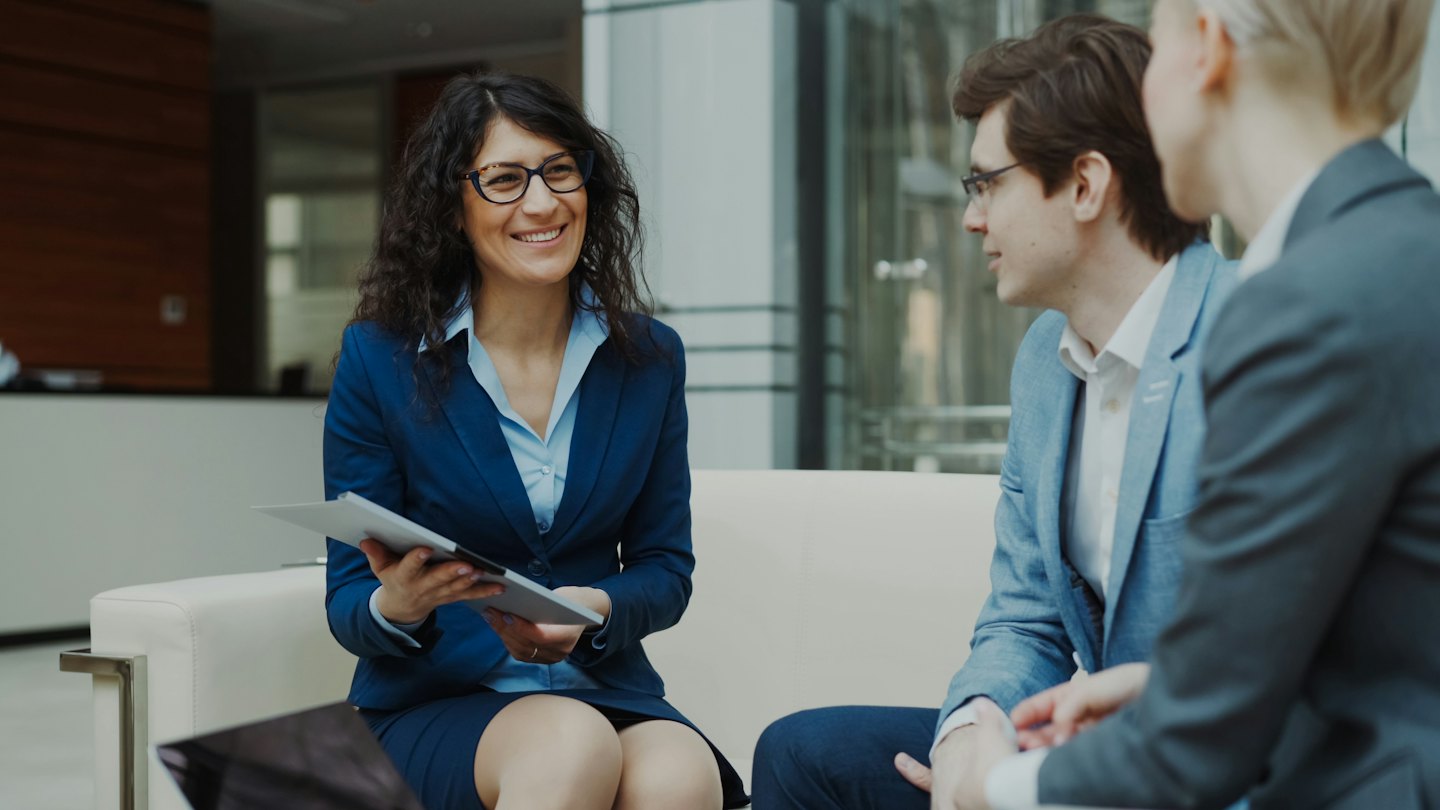 Woman leads business discussion with tablet in modern office lobby.